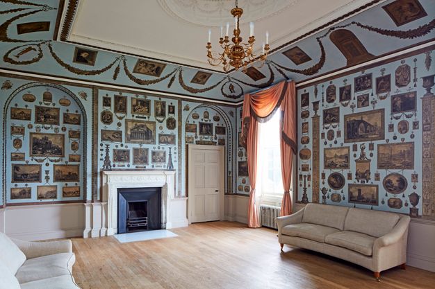 Installation. Dozens of black and white prints in square, rectangular, oval, round, and other formats are pasted to pale blue walls in an elegantly panelled room. More are affixed to the upwards curving cove that connects the wall to the tray ceiling.